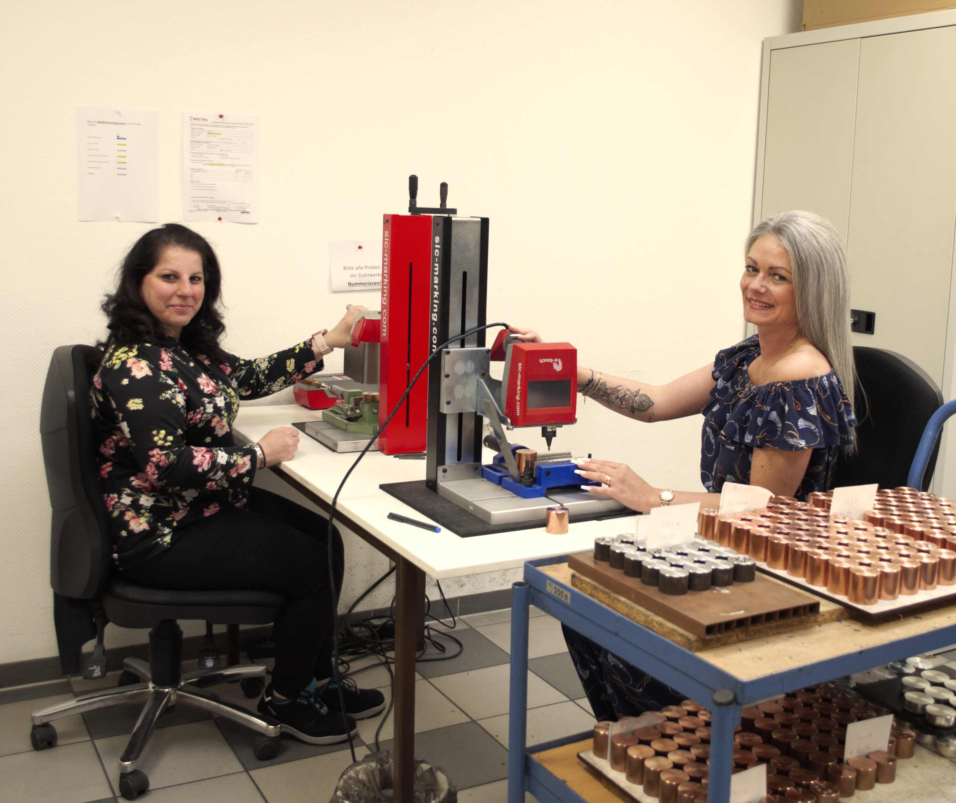 Zu sheen ist ein Büroraum mit zwei Mitarbeiter. Sie bereiten gerade die Kokillenproben für die Nutzung vor und schauen freundlich in die Kamera.
